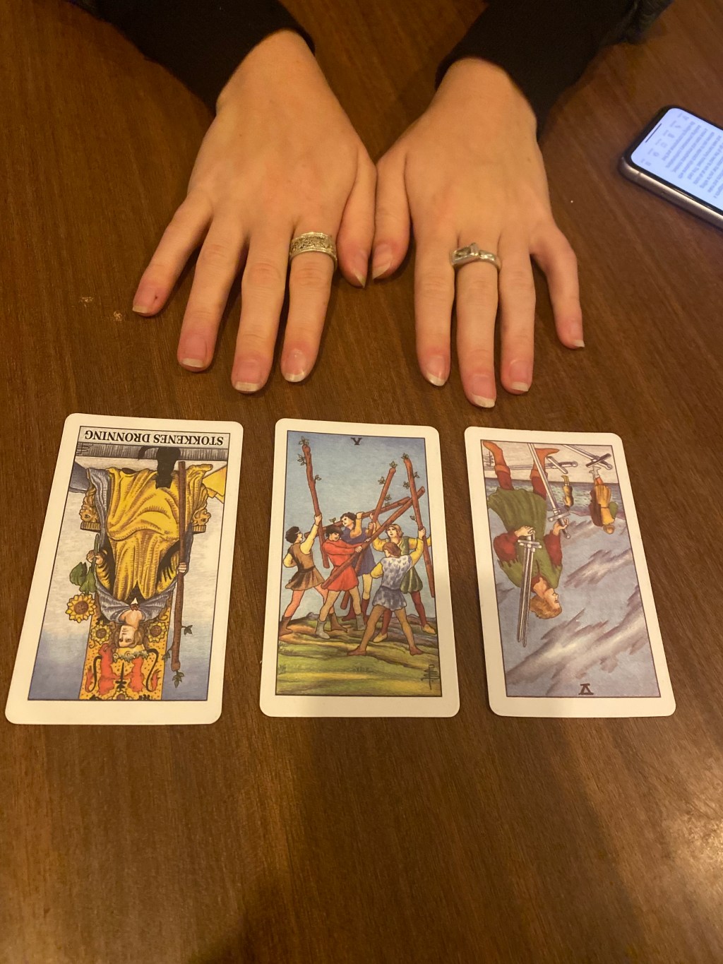 Das Bild zeigt eine Tablettarot-Lesung mit einer Frau, deren Hände in der Mitte des Bildes gezeigt werden, und drei Tarotk...